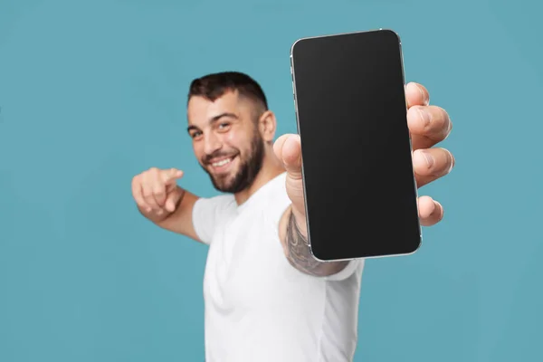 Lächelnder erwachsener europäischer Kerl zeigt Finger am Telefon mit leerem Bildschirm und empfiehlt Gadget — Stockfoto