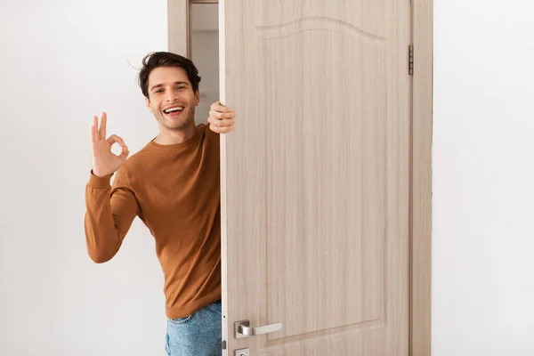 Ragazzo allegro guardando fuori dalla porta mostrando gesto ok — Foto Stock