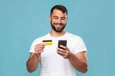 Neşeli orta yaşlı yakışıklı Avrupalı erkek mal sipariş ediyor, kredi kartı ve akıllı telefon gösteriyor.