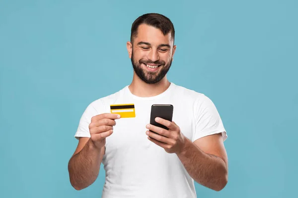 Fröhlicher gutaussehender Mann mittleren Alters bestellt Waren, zeigt Kreditkarte und Smartphone — Stockfoto