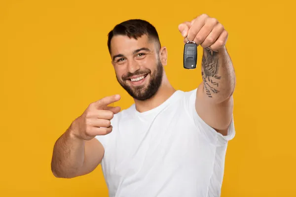 Mutlu gülümseyen, beyaz tişörtlü yakışıklı Avrupalı adam yeni arabanın anahtarlarına parmağını gösteriyor. — Stok fotoğraf