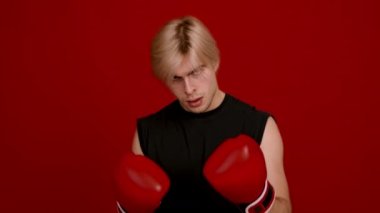 Genç agresif adam kickboksör boks eldivenleri giyiyor, el sıkışıyor, kameraya bakıyor, dövüşmeye hazır.