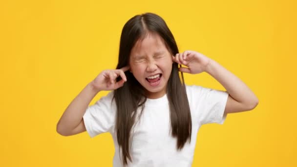 Niegrzeczny mały Azji dziewczyna zatykanie uszy z palce żółty tło — Wideo stockowe