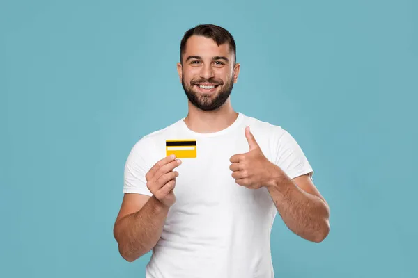 Heureux adulte attrayant homme européen montrant carte de crédit et pouce vers le haut isolé sur fond bleu — Photo