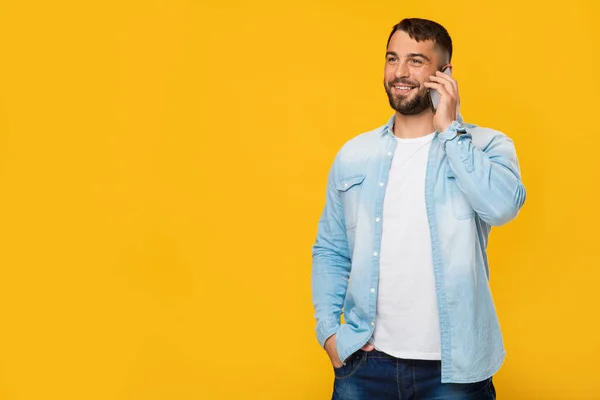 Sakallı neşeli, yakışıklı, Avrupalı bir adam sarı arka planda izole bir şekilde telefonla konuşuyor. — Stok fotoğraf