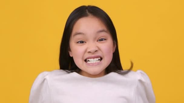 Anak anak marah. Emosional gadis Asia kecil berteriak ke kamera, mengekspresikan emosi negatif oleh jeritan, latar belakang oranye — Stok Video