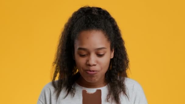 Щаслива афроамериканська дівчина підліток їсть шоколад на жовтому тлі — стокове відео
