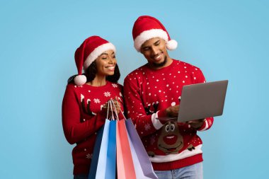 Gülümseyen siyah alışverişkolikler Noel satışlarından keyif alıyorlar, dizüstü bilgisayar kullanıyorlar.
