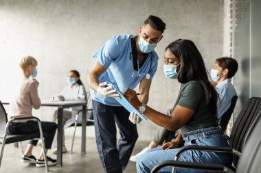 Yüzünde maske olan Afrikalı Amerikalı kadın sağlık raporlarını dolduruyor.