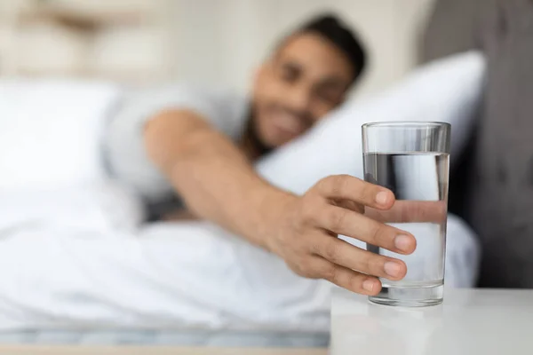 Jonge Arabische man neemt glas water van nachtkastje in de ochtend — Stockfoto