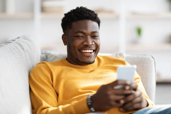 Mosolygó afro-amerikai férfi fekszik a kanapén mobiltelefonnal — Stock Fotó