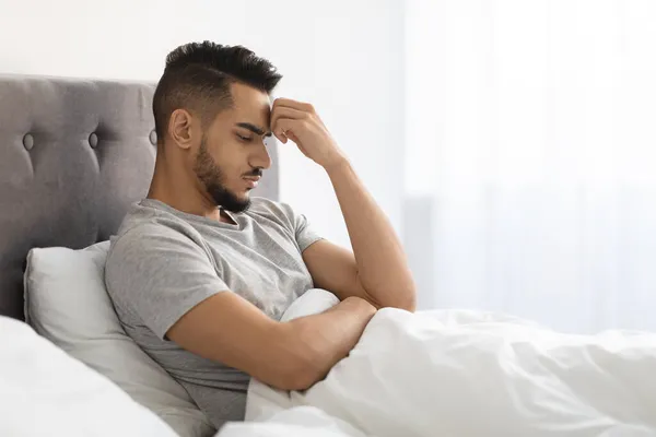 Depressionskonzept. Aufgebrachter junger arabischer Mann sitzt im Bett und denkt über Probleme nach — Stockfoto