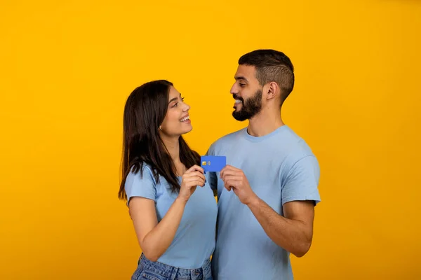 Amantes cónyuges árabes abrazando y mostrando tarjeta de crédito, recomendando servicio bancario sobre fondo amarillo —  Fotos de Stock