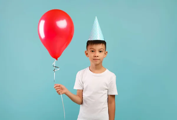 Portret uroczego małego azjatyckiego chłopca noszącego kapelusz Party Holding Red Balloon — Zdjęcie stockowe