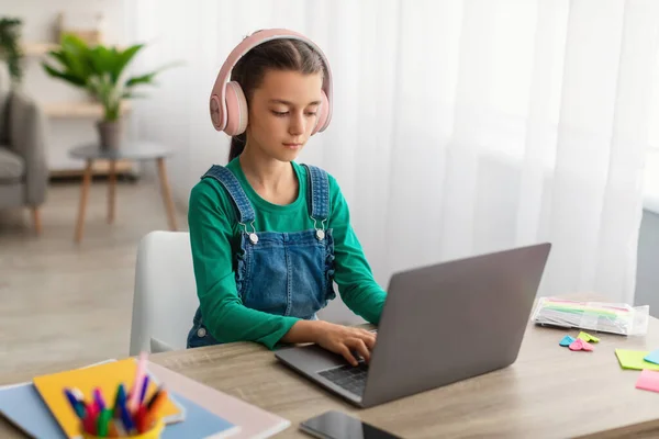 Menina sentada à mesa usando laptop, usando fone de ouvido — Fotografia de Stock