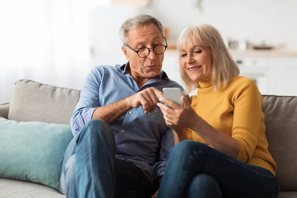 Casal sênior usando mensagens de texto de celular e navegação na Internet em casa — Fotografia de Stock