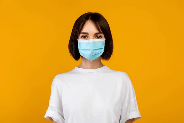 Koncept ochrany proti virům. Portrét dámy v lékařské masce izolované na pastelově oranžovém pozadí, prapor — Stock fotografie