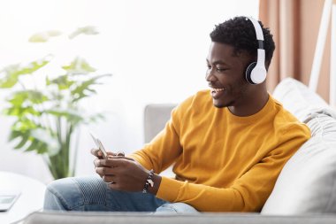 Mutlu siyah adam koltukta oturuyor, cep telefonuyla film izliyor.