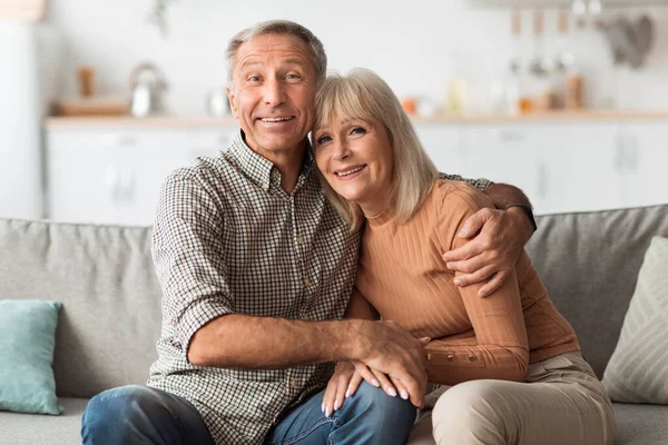 Szczęśliwy mąż starszy i żona przytula uśmiechnięty do kamery w domu — Zdjęcie stockowe