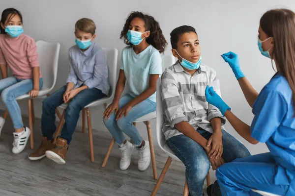 Trabajador médico que hace la prueba de PCR para los niños sentados en la clínica — Foto de Stock