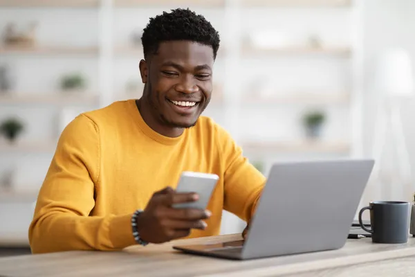 Genç siyahi girişimci dizüstü bilgisayarda çalışıyor ve cep telefonu kullanıyor. — Stok fotoğraf
