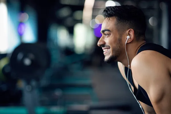 Playlist For Sport. Homem árabe sorridente ouvindo música em fones de ouvido no ginásio — Fotografia de Stock