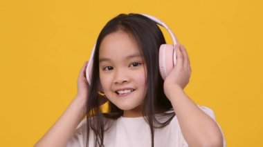 Çocuklar için hediyeler. Sevimli Asyalı kız kablosuz kulaklıkla müzik dinliyor, dans ediyor ve kameraya gülümsüyor.