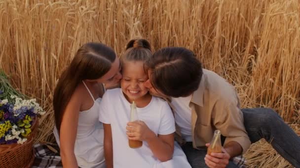 พ่อแม่ที่รักจูบลูกสาวของพวกเขาในขณะที่มีปิกนิกในสนามข้าวสาลีด้วยกัน — วีดีโอสต็อก