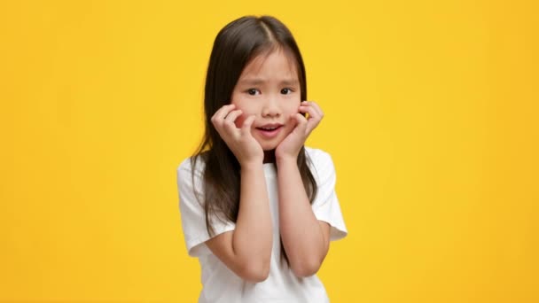 Смешная маленькая японская девочка позирует трогательным лицом над жёлтым фоном — стоковое видео