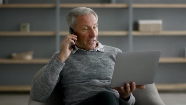 Απομακρυσμένη επιχείρηση. Ηλικιωμένος κύριος χρησιμοποιώντας Laptop και μιλώντας στο κινητό τηλέφωνο στο σπίτι — Αρχείο Βίντεο