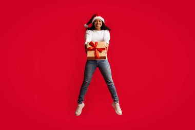 Kırmızı Noel Baba şapkalı duygusal siyah bayan hediyeyle atlıyor.
