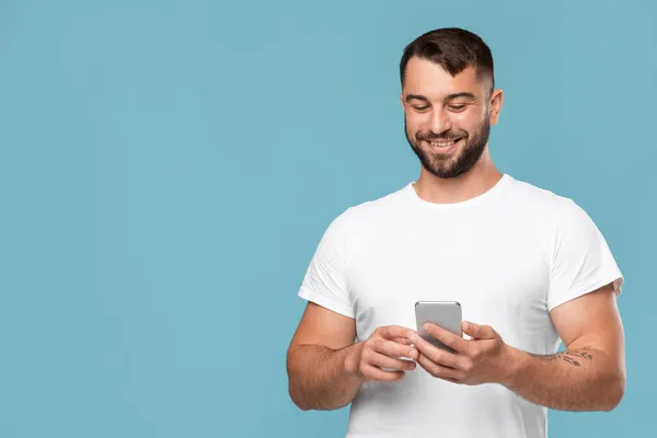 Pria Kaukasia dewasa yang ceria mengetik pesan di smartphone yang terisolasi di latar belakang biru — Stok Foto