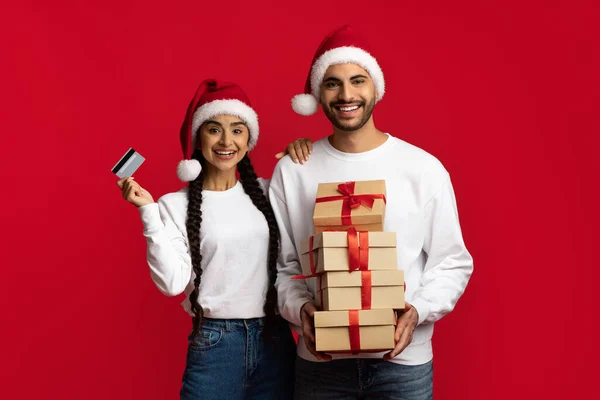Christmas Shopping. Excited Arab Couple With Credit Card And Stack Of Gifts — Stock Photo, Image