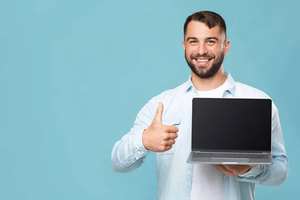 Sorrindo de meia-idade caucasiano cara mostrar laptop com tela vazia e polegar para cima isolado no fundo azul — Fotografia de Stock