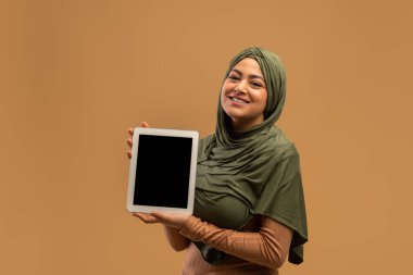 Siyah ekranlı dijital tablet tesettürlü Arap kadının ellerinde, gülümsüyor ve tasarım için alan yaratıyor.
