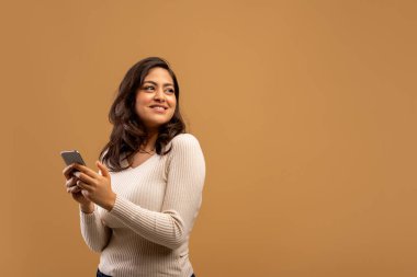 Mobil teklif. Arap kadın akıllı telefonu tutuyor ve boş alana bakıyor, kahverengi arka plan üzerinde duruyor, boş alan.