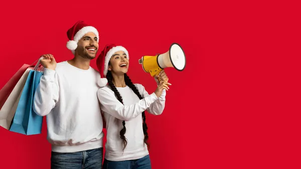 Noel indirimi. Noel Baba Şapkalı Mutlu Arap Çift Megafonla Duyuru Yapıyor — Stok fotoğraf