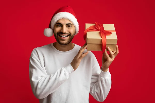 Wesołych Świąt. Ekscytowany Arab Guy w Santa kapelusz gospodarstwa opakowane Present Box — Zdjęcie stockowe