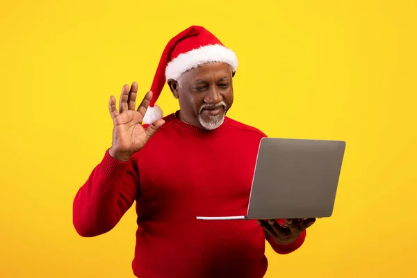 Uomo anziano di colore che fa videochiamate sul computer portatile, indossa il cappello di Babbo Natale, celebra Natale a distanza, comunica online — Foto Stock