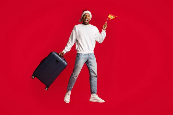 Cheerful black guy holding flag of Spain and suitcase — Stock Photo, Image