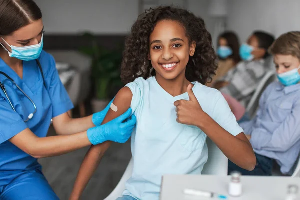 Veselý vakcinované černošky preteen dívka gestikulace palce nahoru do kamery vnitřní — Stock fotografie