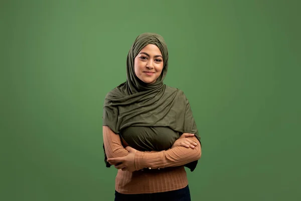 Konsep kecantikan Muslim. Potret wanita arab muda berpose jilbab dengan lengan terlipat di atas latar belakang hijau tua — Stok Foto