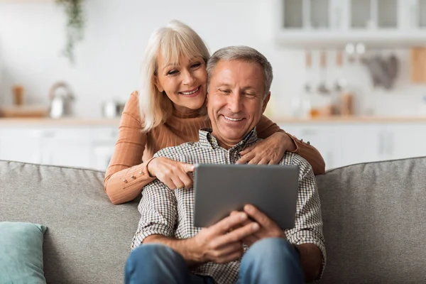 Starší pár pomocí digitálního tabletu počítač sedí na pohovce vnitřní — Stock fotografie