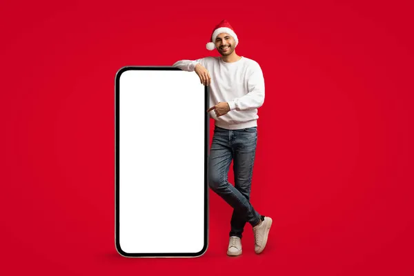 Promoción en línea. árabe chico en santa gorra señalando en grande en blanco Smartphone —  Fotos de Stock