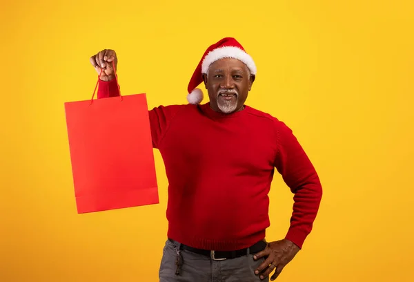 Hombre negro senior positivo en Santa hat sosteniendo bolsa de regalo de Navidad con maqueta para el diseño del logotipo de la marca sobre fondo naranja — Foto de Stock