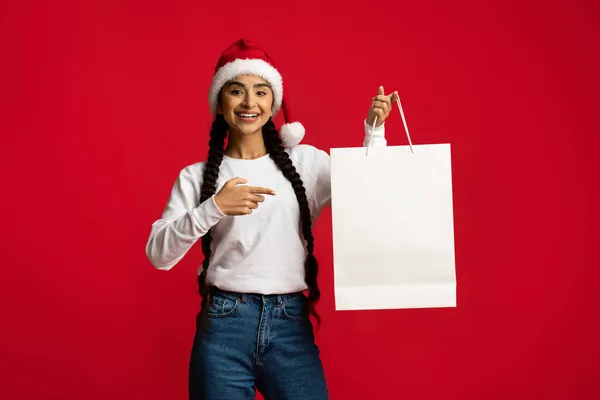 Šťastná arabská žena v Santa Klobouk ukazující na prázdný papír nákupní taška — Stock fotografie
