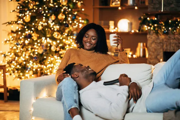 Любимая чернокожая женщина проводит время со своим счастливым бойфрендом в канун Рождества в украшенной гостиной, копировать пространство — стоковое фото