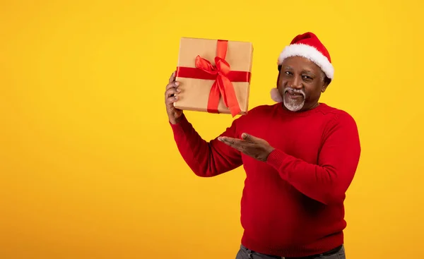 Retrato navideño de un hombre negro jubiloso con sombrero de Santa Claus sosteniendo un regalo de Navidad sobre fondo naranja, espacio vacío — Foto de Stock