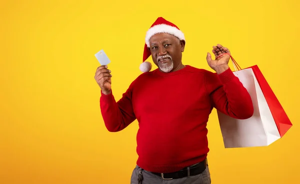 Kerstverkoop en winkelen. Senior zwarte man met shopper tassen met credit card, het dragen van Santa hoed — Stockfoto