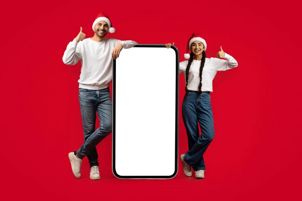 Vilken bra app. Glada par bär Santa Hattar Stående Nära Big Blank Smartphone — Stockfoto
